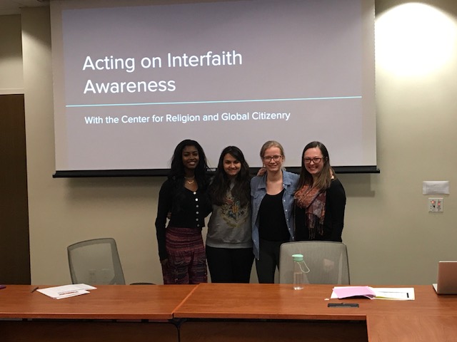 Four interfaith fellows posing in front of a presentation that they are facilitating titled "Acting on Interfaith Awareness" at the New People, New Voices Seminar. 